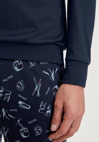 Marineblauw langemouwen top en gestreepte broeken met skis, een koe en een eekhoorn in witte en rode accenten. Glad materiaal, nauwsluitend design.