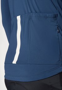 Haut de sport bleu marine avec une poche zippée latérale, présentant une bande blanche le long du bas. Fabriqué en tissu lisse et fonctionnel.