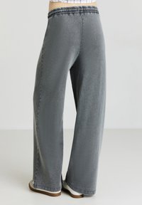 Pantalons large gris avec une taille élastique. Le tissu a une texture douce, avec un léger éclat et des poches latérales.