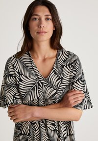 Abito corto a maniche corte in bianco e nero con scollatura a V e motivo a foglie, dalla vestibilità comoda e con dettaglio della vita arricciata.