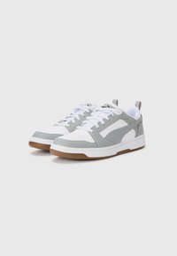 Grå og hvid sneakers med en glat læderoverdel, perforeret tåområde, flade hvide snørebånd og en gummisål med brune accenter.