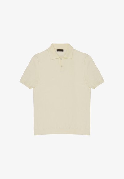 Jasnobeżowa koszulka polo z krótkim rękawem, z ściągaczem na dole, plisą na dwa guziki i szpiczastym kołnierzykiem, rozłożona płasko na białym tle.