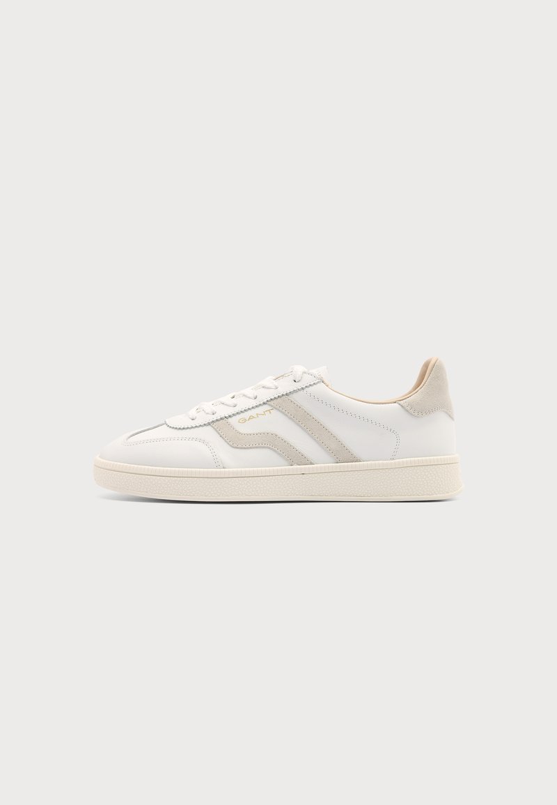 Baskets basses blanches avec détails en daim beige et lacets blancs, dotées d'une semelle texturée et d’un marquage discret sur le côté.