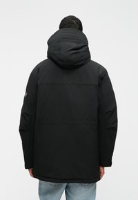 Casaco preto com capuz, com um corte descontraído, apresentando uma textura suave, um design minimalista e detalhes de costura visíveis nas costas.