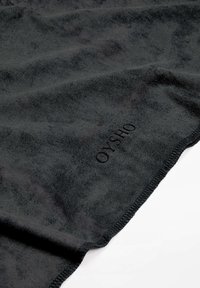 Črna plišasta odeja iz mehkega blaga z gladko teksturo. Ima šivani rob in tudi embosirano logo v enem kotu.