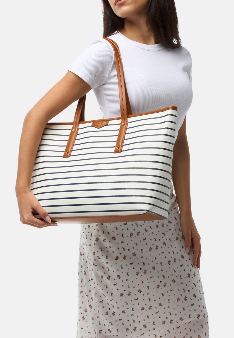 Striped tote bag with a white and navy pattern, brown leather handles and trims, spacious design, textured surface, and reinforced base.