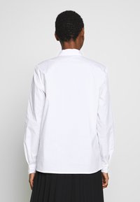 Vit långärmad skjorta i bomull, med rak skärning, knäppta manschetter och klassisk krage. Bakvyn visar en slät textur.