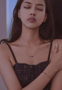 Collar de oro con la palabra "amor" y un colgante en forma de corazón azul; pulsera de oro a juego también con un acento azul; modelo lleva un atuendo negro.