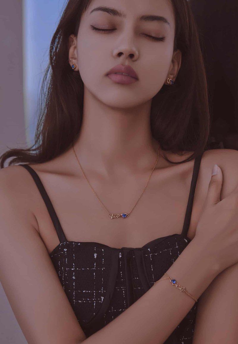 Collar de oro con la palabra "amor" y un colgante en forma de corazón azul; pulsera de oro a juego también con un acento azul; modelo lleva un atuendo negro.