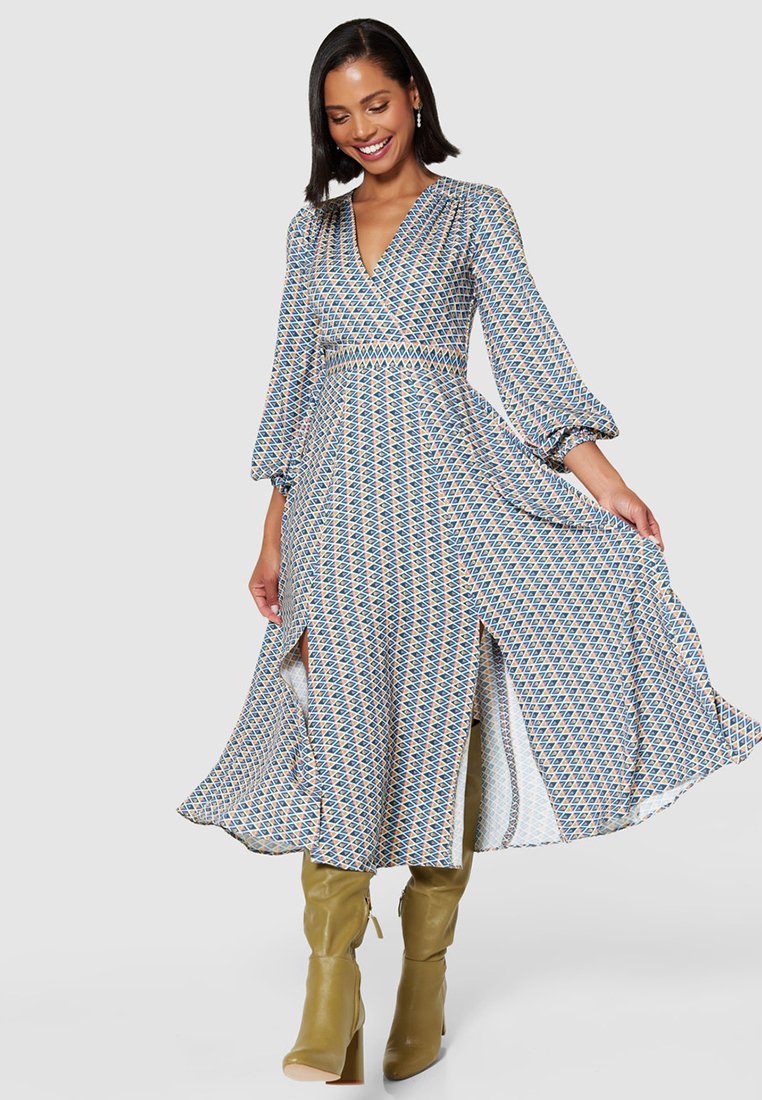 Długa, wzorzysta sukienka z dekoltem w szpic, bufiastymi rękawami i bocznymi rozcięciami. Wykonana z lekkiego materiału, przedstawiającego niebieskie, pomarańczowe i kremowe geometryczne wzory.