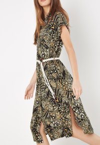 Vestito a stampa floreale verde scuro, maniche corte, fessure laterali e una cintura in corda annodata. Presenta motivi intricati e un tessuto leggero.