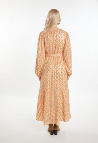 Rochie maxi de culoare portocalie cu un model floral, mâneci lungi tip puff, talie strânsă și tiv cu volane, asortată cu cizme cu toc maro.