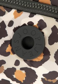 Tkanina w panterkę z beżowymi, brązowymi i czarnymi plamami; zawiera okrągły czarny gumowy akcent z wypukłymi literami i siateczkowym środkiem.