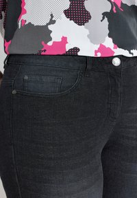 Jeans en denim noir avec une taille mi-haute, deux poches avant et une seule poche arrière agrémentée d'un détail en bouton argenté.