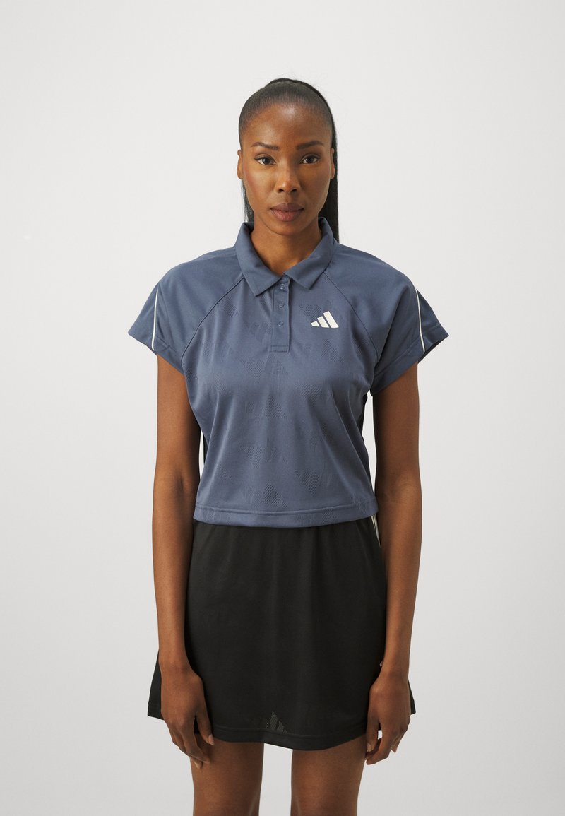 Námornícky skrátený pólový tričko s krátkymi rukávmi, textúrovaná tkanina a biele logo na hrudi, spárované s čiernou sukňou.