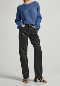 Jasnoniebieski sweter z dzianiny o otwartym splotem i napisem, w połączeniu z czarnymi dżinsami z wysokim stanem o prostym kroju oraz czarnymi sandałami na obcasie z paskami.