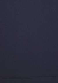 Temno modra bombažna tkanina, gladke teksture, s doslednim pletenim vzorcem. Ima raven rob na dnu z vidnimi šivi.