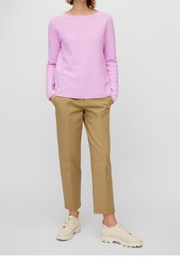 Suéter de manga larga de color rosa claro con cuello redondo, combinado con pantalones beige a medida y zapatillas blancas hueso, con tejido texturizado.