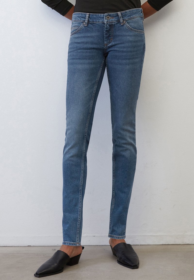 Chude niebieskie dżinsy wykonane z denimu, charakteryzujące się klasycznym pięciokomorowym wzorem, wyblakłym odcieniem i subtelnymi detalami w szwie, w zestawieniu z czarnymi klapkami.