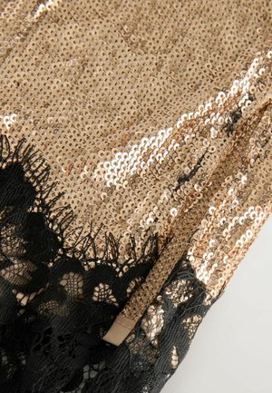 Goldene Paillettenstoff mit einer glänzenden Oberfläche, versehen mit einem zarten schwarzen Spitzenrand an einer Kante. Das Design ist glatt und reflektierend.