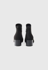 Stivali alla caviglia in suede nero con punta rotonda, tacco a blocco basso e cerniera laterale. Texture liscia e senza motivi visibili o dettagli hardware.