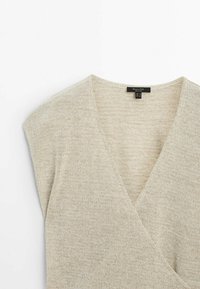Light beige knitted top with a V-neck design and short sleeves. The texture is soft and slightly loose-knit. Includes a label at the neckline.