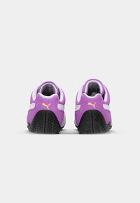 Violetti urheilukengät, joissa on teksturoitu pinta, valkoisia yksityiskohtia ja musta kumipohja. Kantapäässä on pieni keltainen logo.
