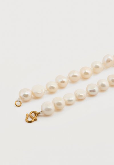 Κοντινή λήψη ενός κολιέ με πέρλες που κλείνει με κούμπωμα, με λευκές πέρλες ακανόνιστου σχήματος και χρυσό γάντζο κούμπωμα σε λευκό φόντο.