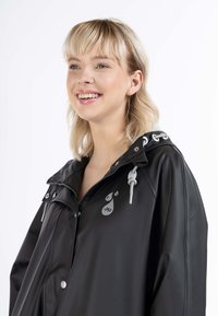 Impermeable negro con capucha ajustable, logo plateado y herrajes plateados. Cuenta con un cierre frontal con cremallera y cierres a presión.