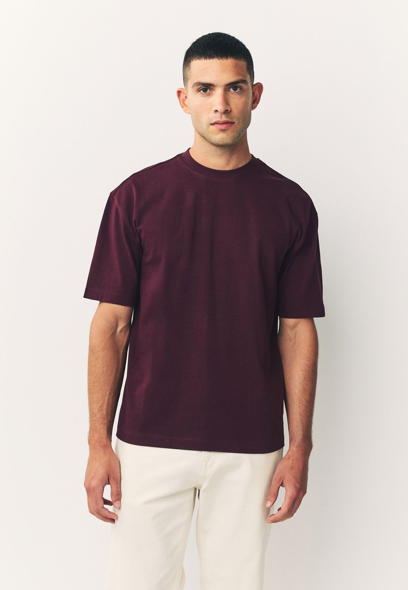 Bordeauxrode katoenen T-shirt met korte mouwen, ronde halslijn en een ontspannen pasvorm. Gladde textuur, minimalistisch ontwerp, zonder zichtbare logo's of patronen.
