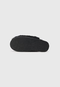 Fekete slip-on cipő, texturált gumitalppal, logóval és bolyhos textile felsőrésszel. A dizájn egyszerű, látható minták nélkül.