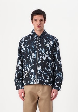 Black and blue patterned jacket with a zip front, pointed collar, and a small logo. The fabric appears smooth and lightweight.