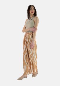 Beige mouwloos topje gecombineerd met een lange, vloeiende rok met een abstract patroon in bruin en room. Platte, neutraal gekleurde schoenen maken de outfit compleet.