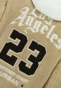 Beige fleece sweater met witte capuchon, met "Los Angeles" en een zwarte "23" in dikke, textuurrijke borduurwerk en kleine gedrukte details eronder.