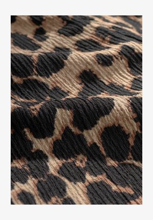 Leopardimustriga kangas, millel on tekstuuriline pind, suured mustad ja beežid laigud beezil taustal, luues lainelise välimuse.