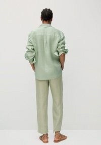 Jasnozielona lniana koszula z podwiniętymi rękawami, zestawiona z dopasowanymi spodniami, charakteryzującymi się luźnym krojem i prostym designem. Całość uzupełniają sandały na paski.