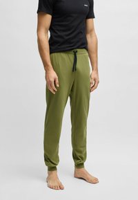 Olijfgroene joggingbroek met een trekkoord in de taille en geribbelde boorden, gecombineerd met een zwarte ronde hals t-shirt. Smooth stoffen textuur.
