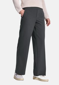 Graue weite Hosen aus glattem Material. Mit seitlichen Taschen und geradem Schnitt, kombiniert mit weißen Sneakers.