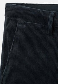 Nahaufnahme von schwarzen Cordhose, die den Bund, die Gürtelschlaufe und die diagonale Naht der Fronttasche zeigt.