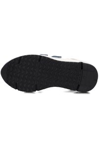 Schwarze Gummisohle mit wellenförmigem Profil, kombiniert mit einer weißen Zwischensohle und blauen textile Akzenten entlang des oberen Randes.