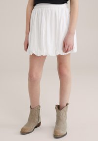 White gathered mini skirt with an elastic waistband, paired with beige ankle boots featuring decorative stitching and a slight heel.