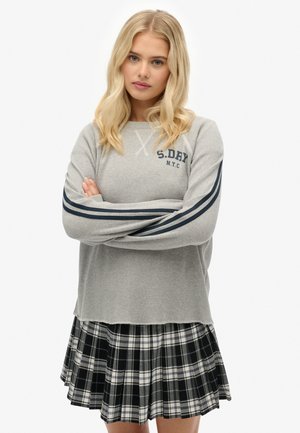 Grå langærmet sweater med ribbet struktur og marineblå striber på ærmerne, kombineret med en sort og hvidternet plisseret nederdel.