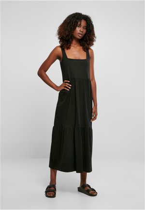 Black sleeveless maxi dress with a square neckline and tiered hem, crafted from soft fabric. Model paired it with dark sandals.