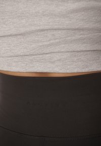 Gray ribbed tank top layered over black high-waisted leggings featuring subtle branding. The fabric appears smooth and stretchy.
