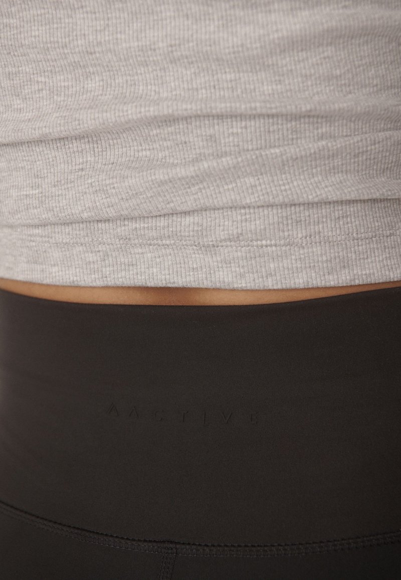 Gray ribbed tank top layered over black high-waisted leggings featuring subtle branding. The fabric appears smooth and stretchy.