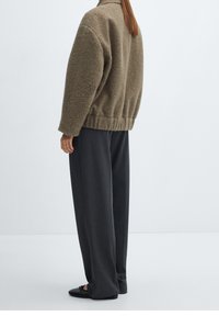 Khaki fleece sweater with a high collar, elastic hem, paired with loose dark trousers and black slip-on shoes. Soft texture, relaxed fit.