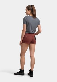 Camicetta grigia a maniche corte abbinata a pantaloni corti color ruggine con un pannello nero. Indossata con sneaker alte nere, vista da dietro.