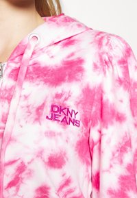 Felpa con cappuccio e zip bianca con motivo tie-dye rosa. Presenta il logo ricamato "DKNY JEANS" in rosa sulla parte sinistra del petto.