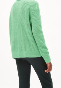 Ljusgrön stickad tröja med lös passform, med ribbat mönster och långa ärmar. Bärs tillsammans med mörka, strukturerade byxor.