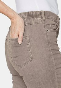 Hellbraune Denim-Jeans mit elastischem Bund, Seitentaschen und tailliertem Schnitt. Die Textur wirkt weich und leicht abgenutzt.